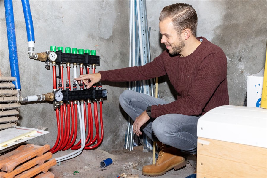 Man zit gehurkt bij een aantal leidingen van een warmtepomp